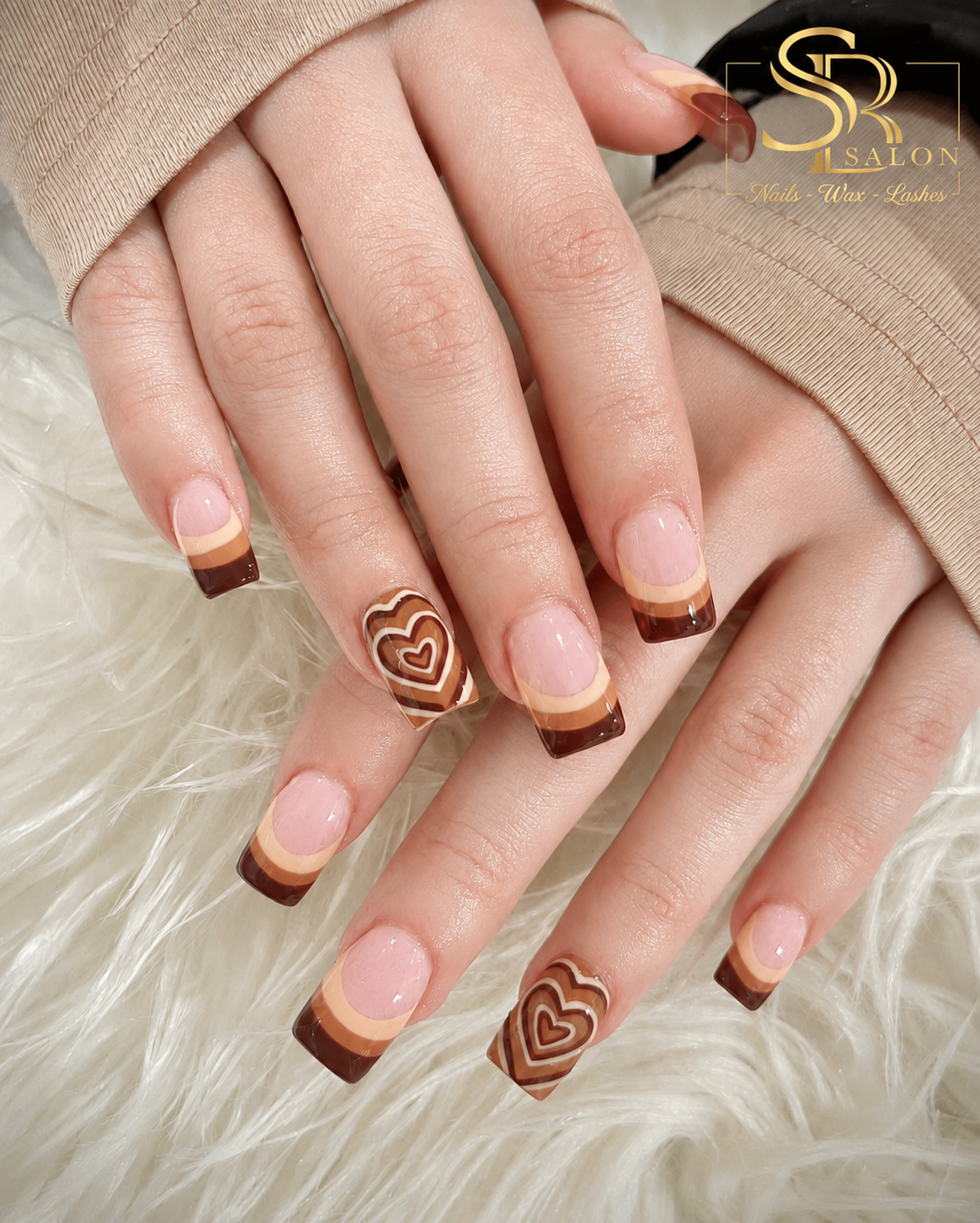 Square nails with layered caramel and brown French tips and heart accent nail art.