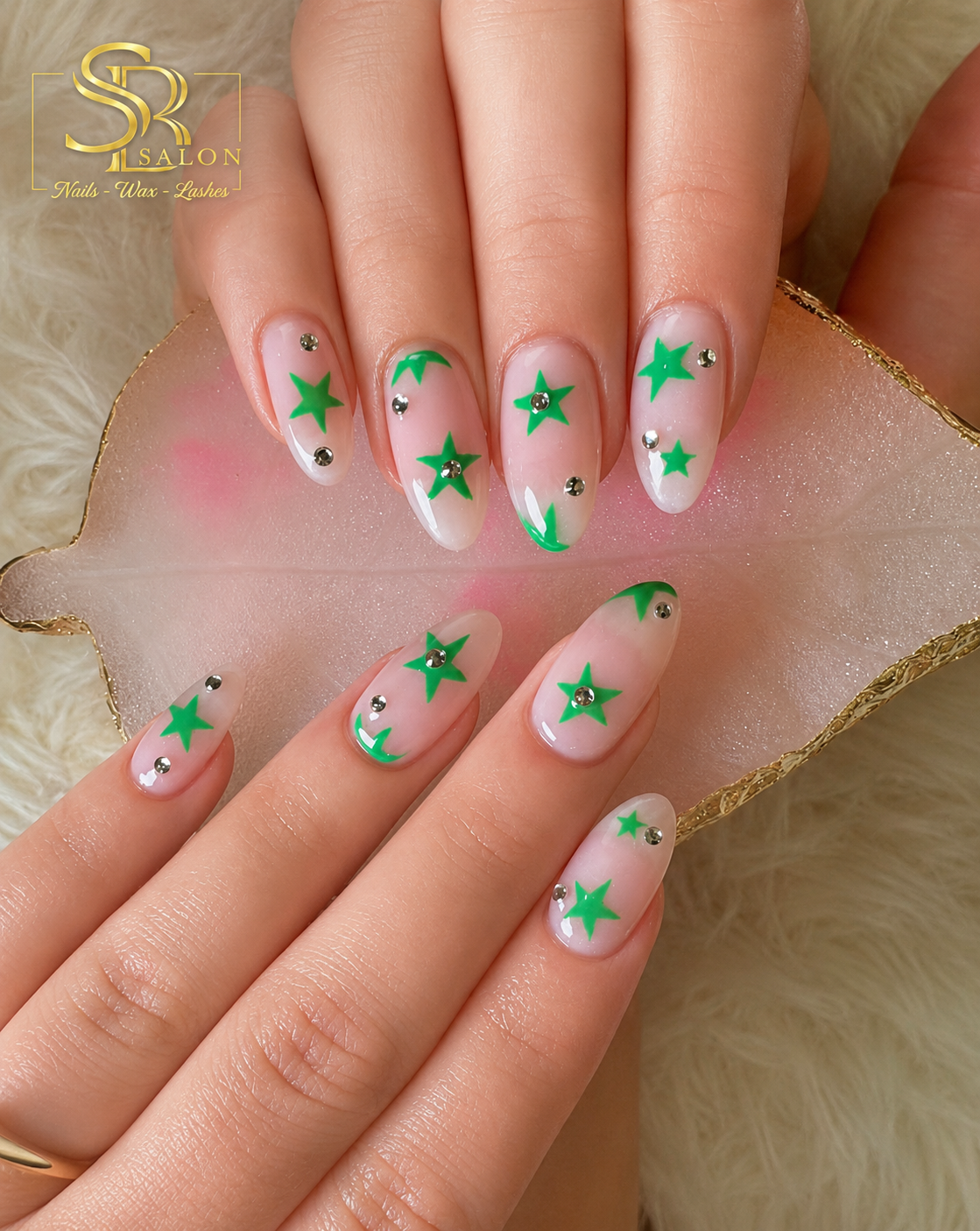Nude almond nails with bright green star nail art and small crystal accents.