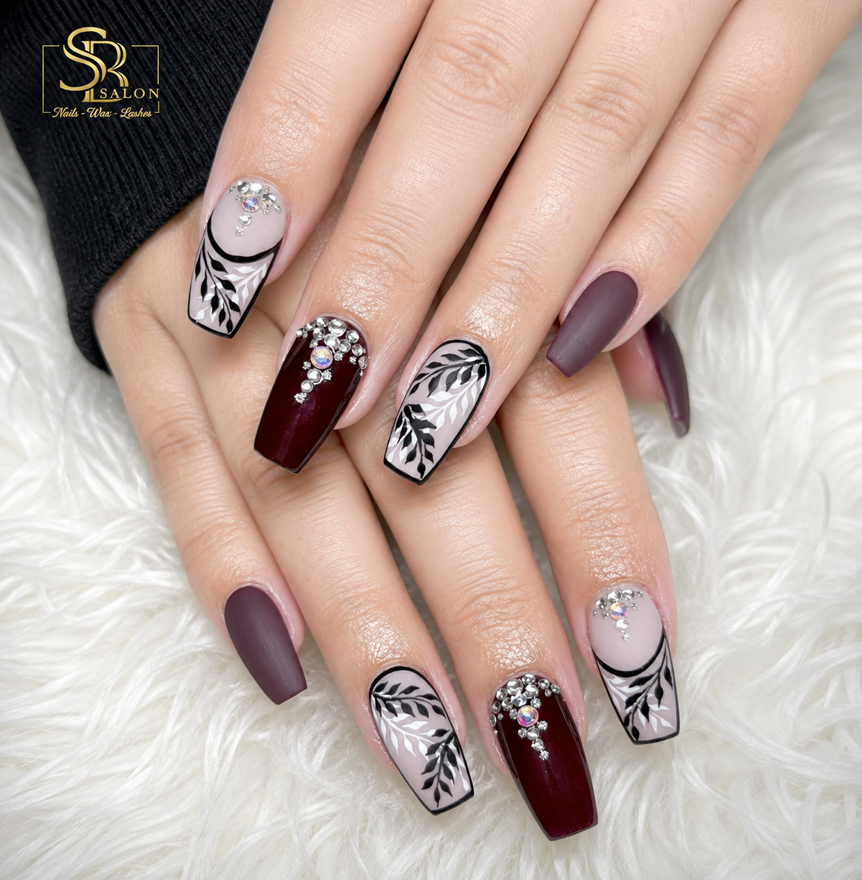 Deep maroon coffin nails with black leaf nail art and silver crystal embellishments.