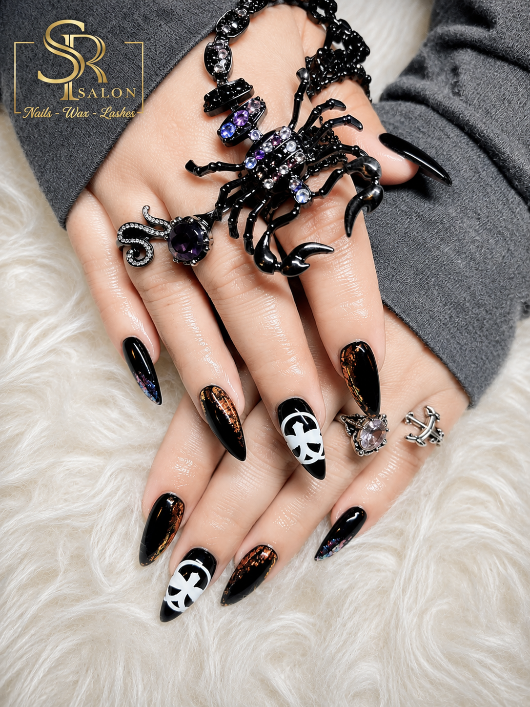 Long stiletto nails in glossy black with gothic cross accents and copper foil detailing.