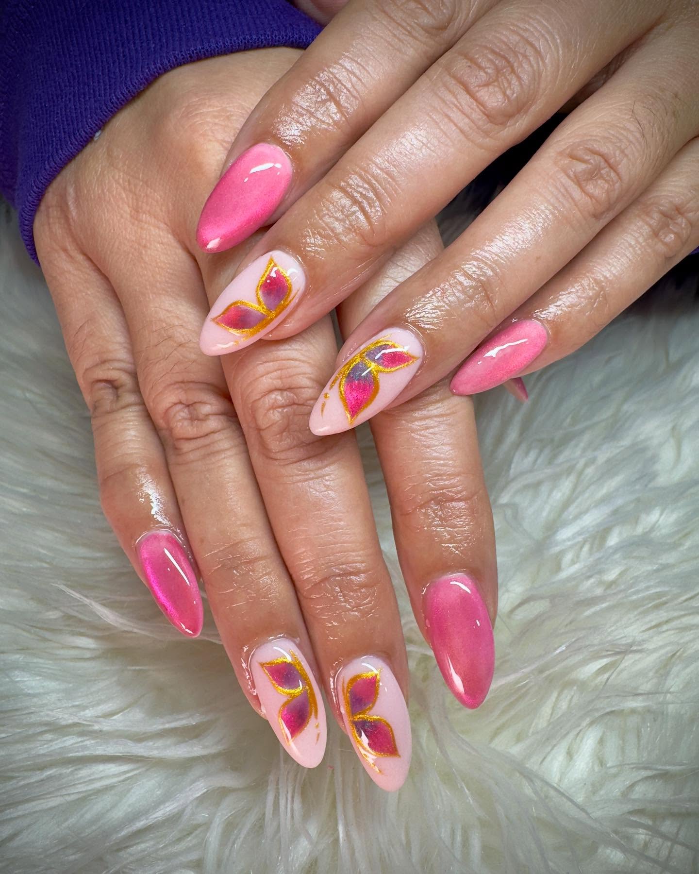 Pink chrome almond nails with gold outlined petal nail art on a soft cream background.