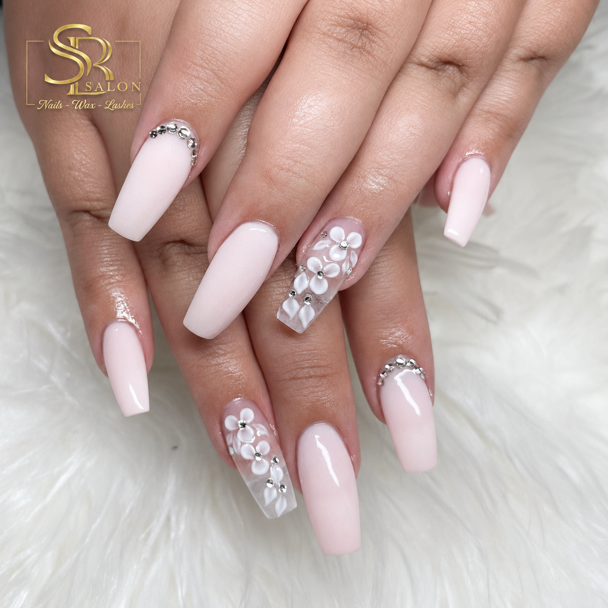 Nude coffin nails with white 3D flowers and crystal accents on a soft faux-fur background.