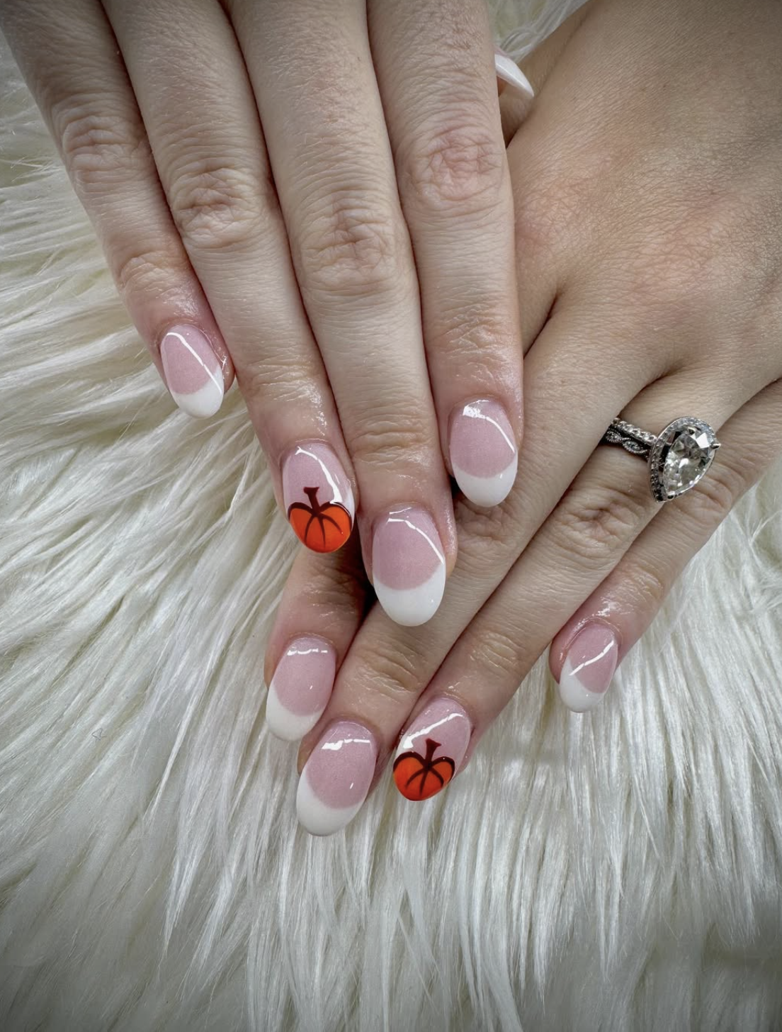 Minimal pink and white French nails with small orange pumpkin art for an autumn look.