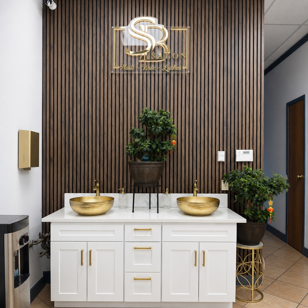 Vanity area with gold vessel sinks and walnut slat wall featuring the gold SB Salon logo.