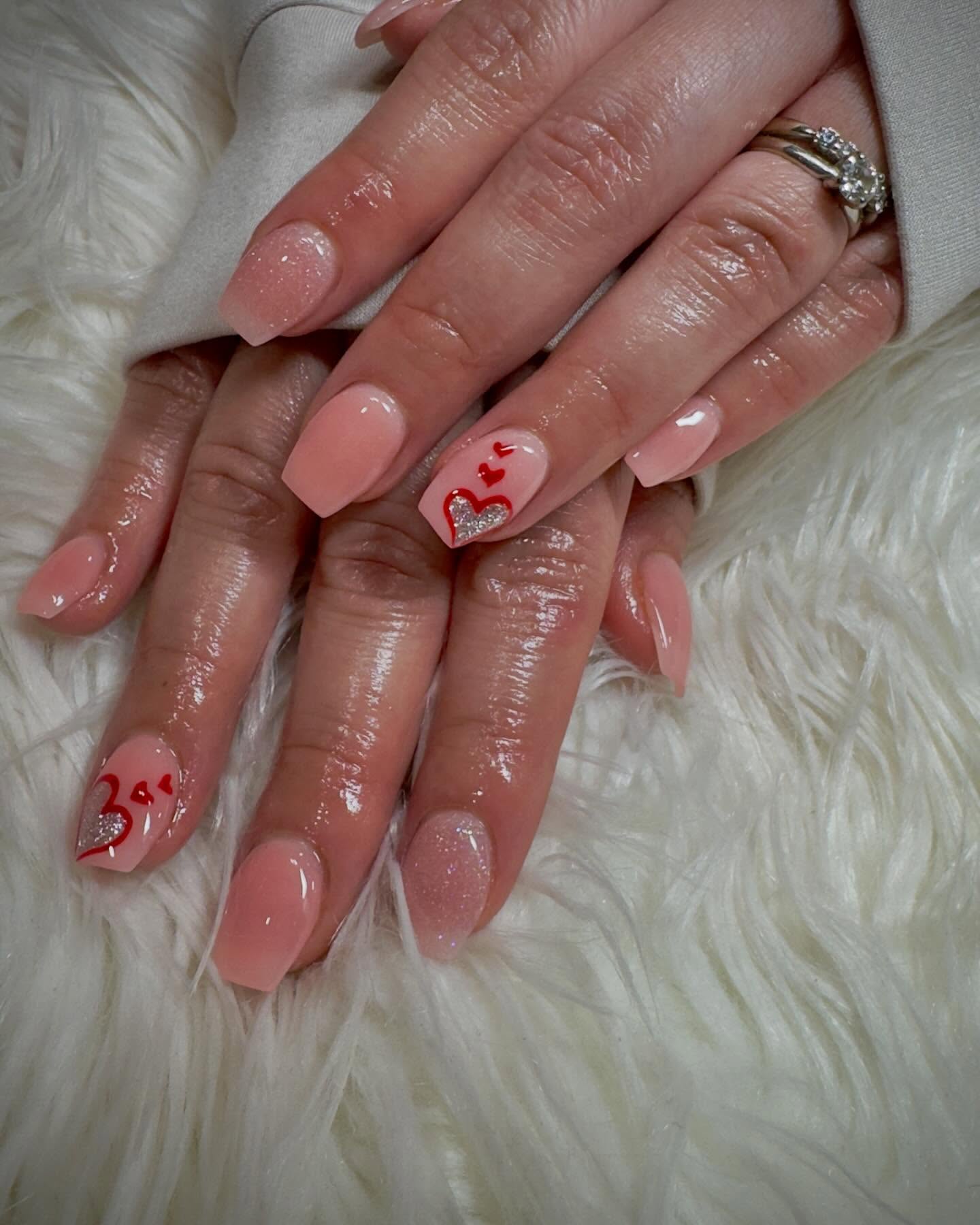 Soft pink nails with glitter accent and red heart nail art photographed on ivory faux fur.