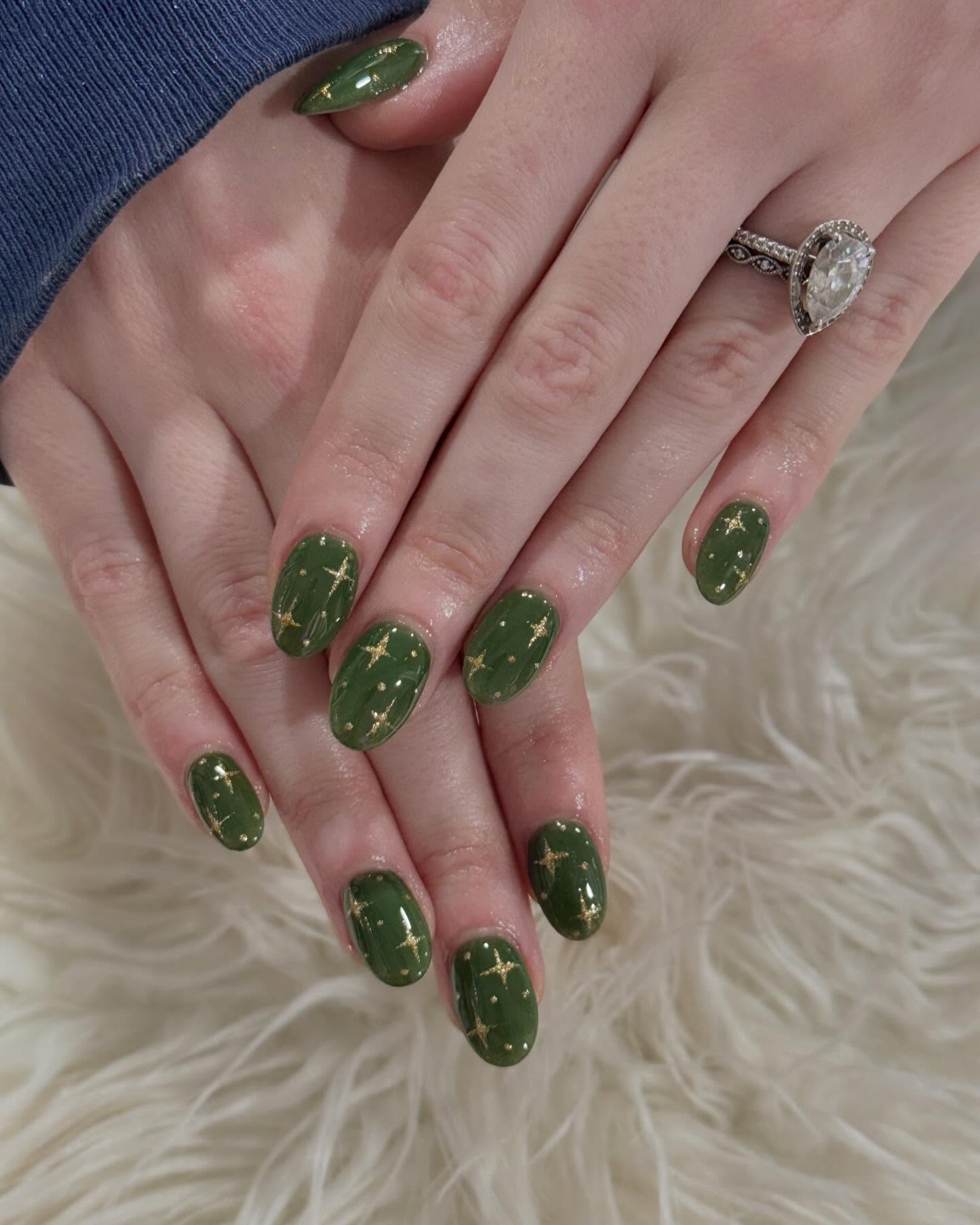 Glossy olive green nails with delicate gold star details in an editorial close-up.