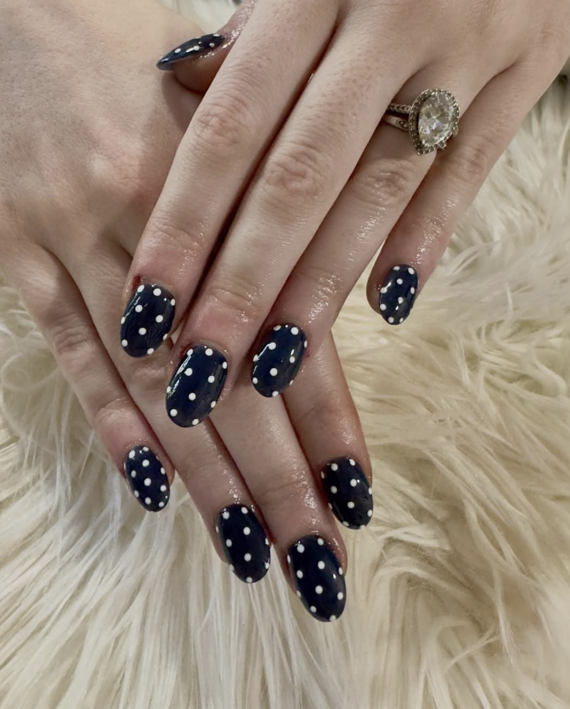 Navy almond nails with crisp white polka dots styled against a soft cream surface.