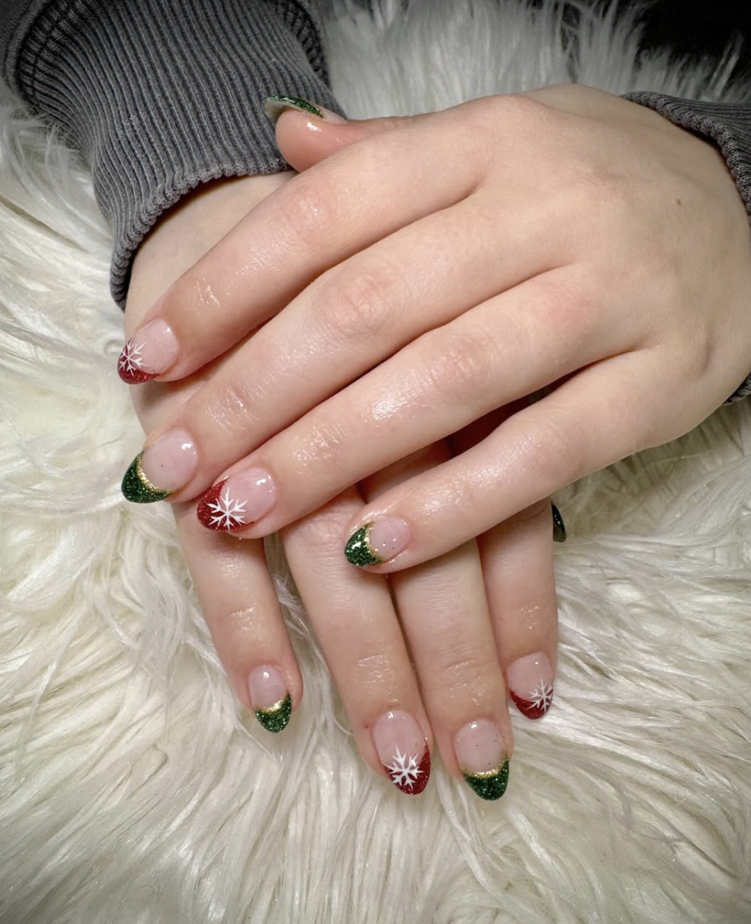 Short natural nails with red and green glitter French tips and white snowflake accents.