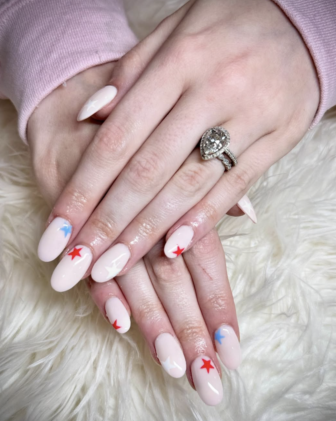 Milky nude almond nails with tiny red, white, and blue stars in a clean editorial style.